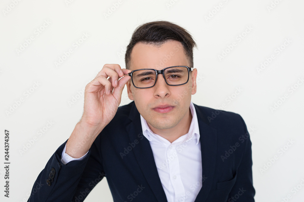 Concerned guy in office clothes staring at camera through eyewear. Young Caucasian man in jacket touching glasses and posing. Sight or vision concept Concerned guy in office clothes staring at camera through eyewear. Young Caucasian man in jacket touching glasses and posing. Sight or vision concept