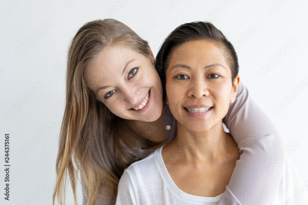 Cheerful women hugging. Closeup of multiethnic lesbian couple posing and smiling at camera. Happy couple concept Cheerful women hugging. Closeup of multiethnic lesbian couple posing and smiling at camera. Happy couple concept