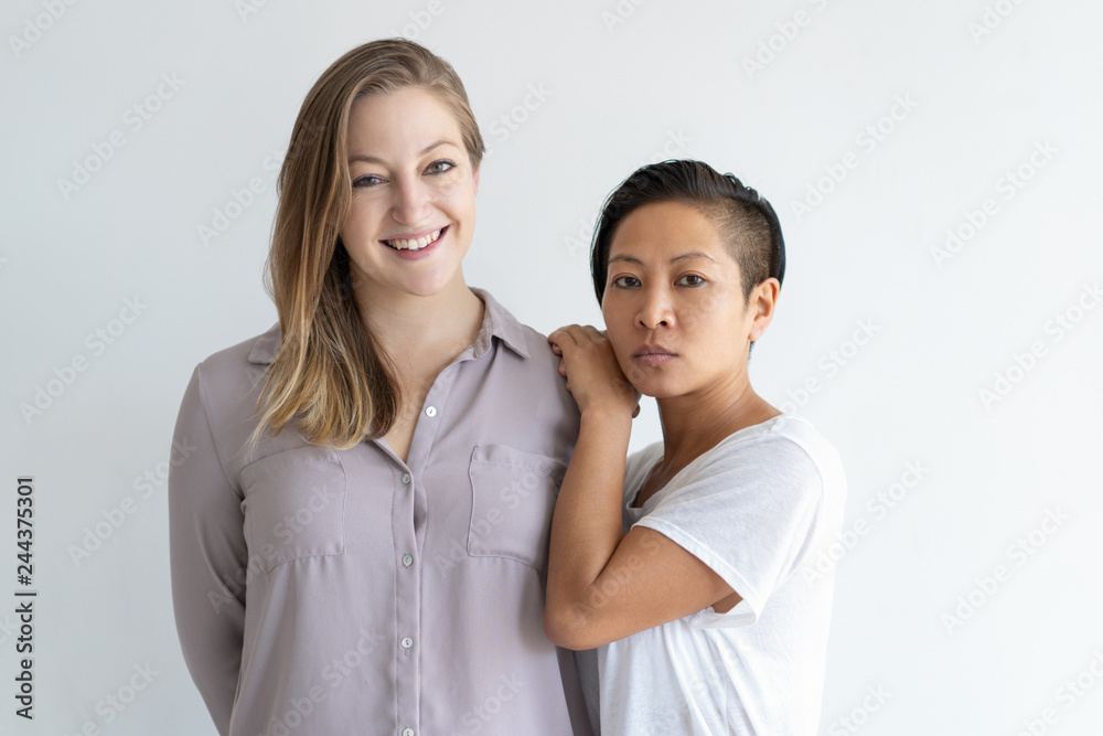 Portrait of mix raced lesbian couple. Serious trendy girl leaning on cheerful girlfriend shoulder. Multiethnic couple concept Portrait of mix raced lesbian couple. Serious trendy girl leaning on cheerful girlfriend shoulder. Multiethnic couple concept