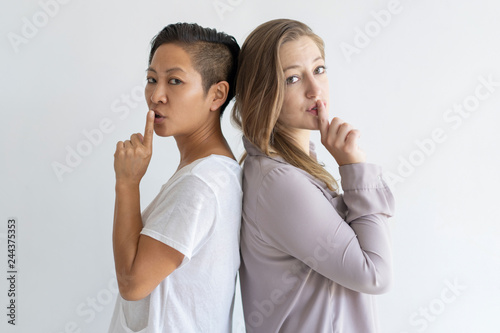 Serious girls keeping secret. Two lesbian women standing back to back and showing shh gesture. Silence concept