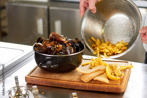 Pouring out french fries from sausepan. Mussels with side dish. photo