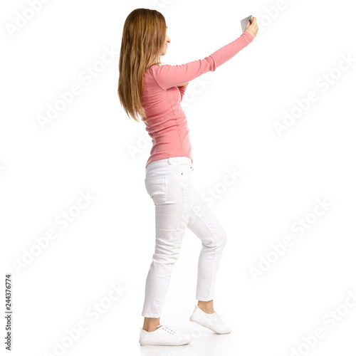 Woman in white jeans and shirt making selfie smartphone on white background isolation, back view