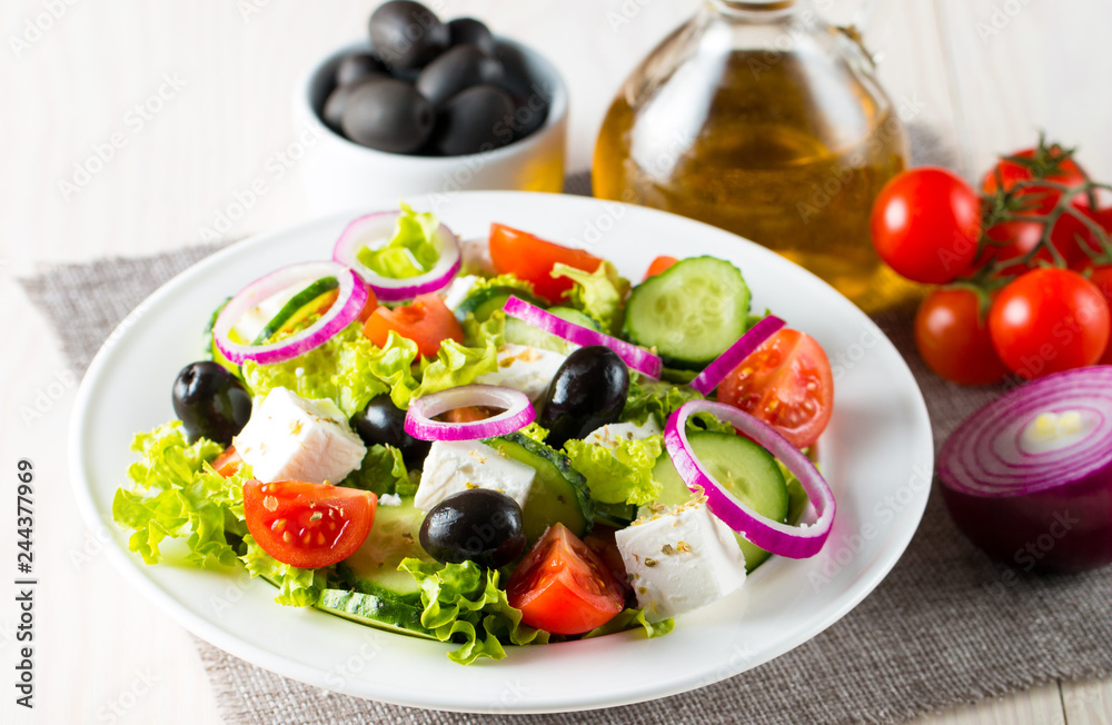 Fresh Greek salad made of cherry tomato, ruccola, arugula, feta, olives, cucumbers, onion and spices. Caesar salad in a white bowl on wooden background. Healthy organic diet food concept.