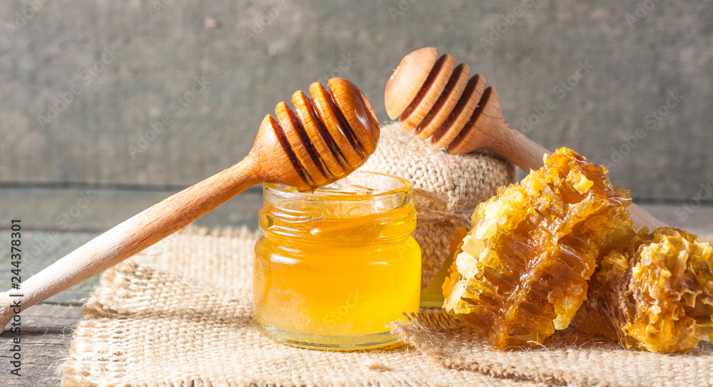 Honey dripping from a wooden honey dipper in a jar on wooden grey rustic background Honey dripping from a wooden honey dipper in a jar on wooden grey rustic background