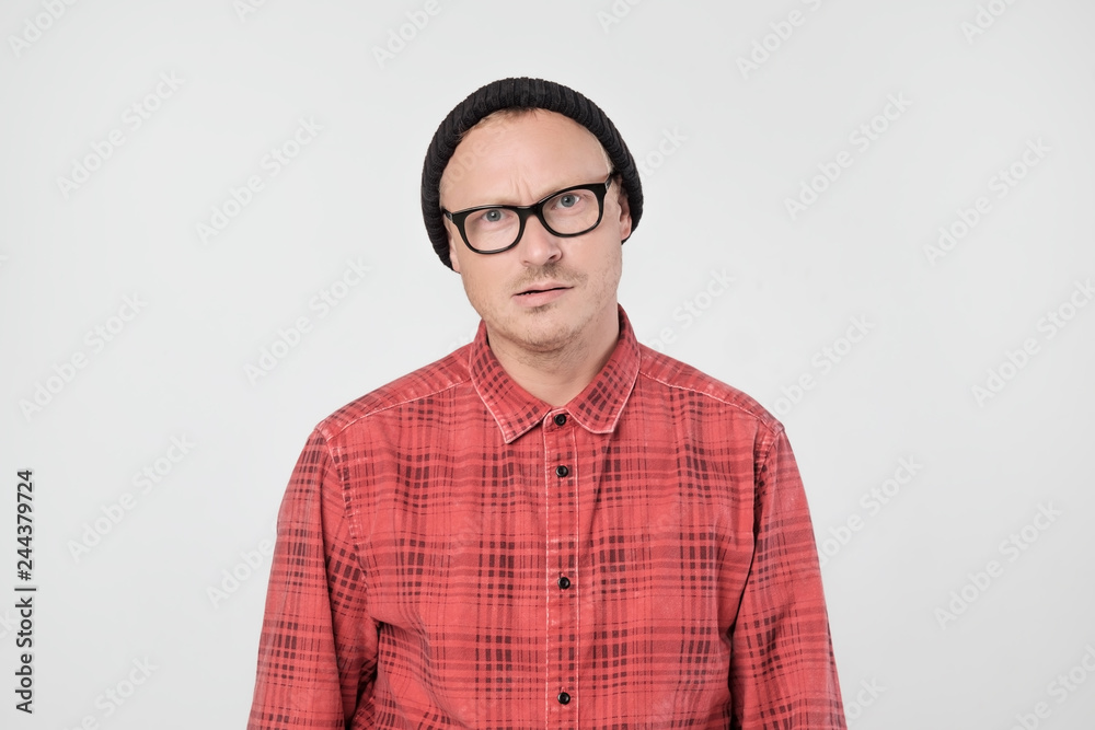 Young european man in red shirt dissatisfied frowns and looks sullenly.