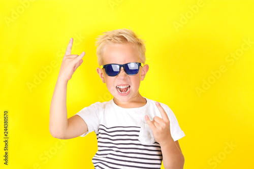 Cute blond boy wearing sunglasses showing Horns gesture