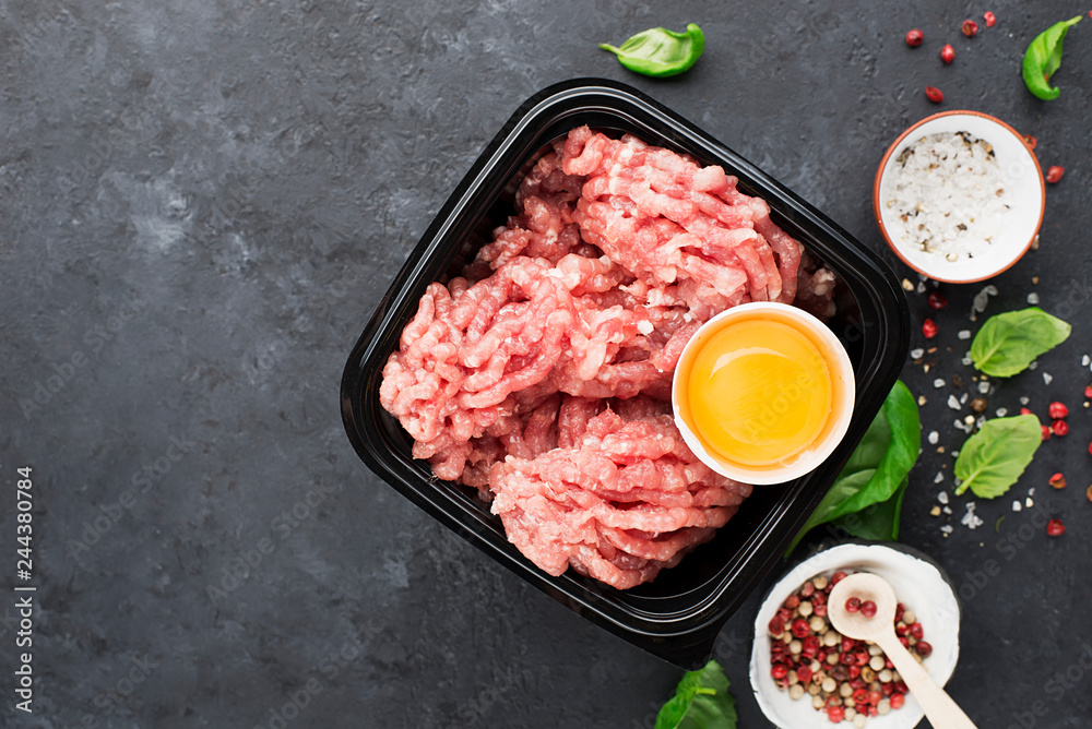 Raw minced meat with salt, pepper, egg, herbs, spices for a burger. On a dark background. Top view.