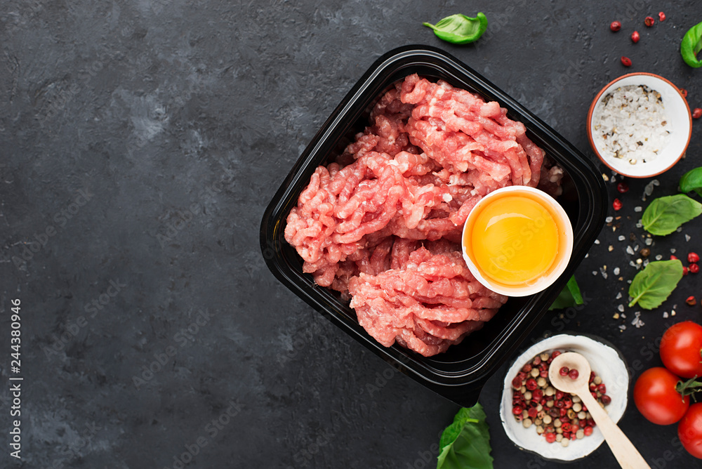 Raw minced meat with salt, pepper, egg, herbs, spices for a burger. On a dark background. Top view. Raw minced meat with salt, pepper, egg, herbs, spices for a burger. On a dark background. Top view.