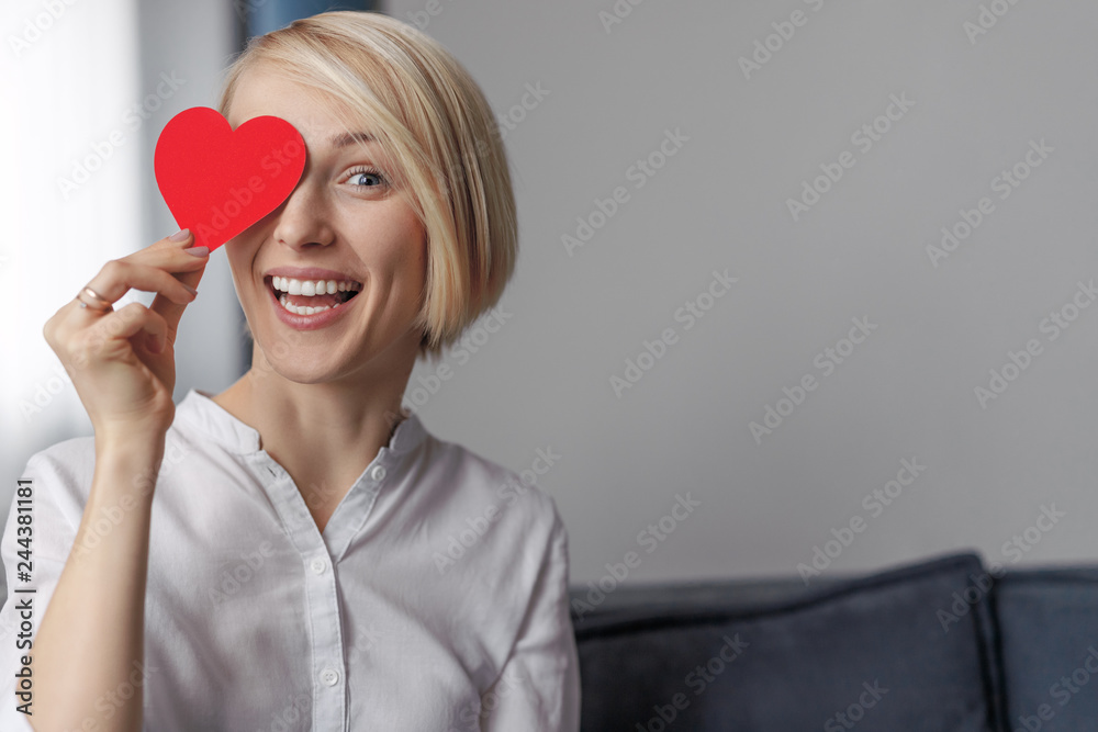 Cheerful lady holding heart near eye