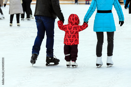 Obraz na płótnie A little boy with his parents skates on the rink in the winter