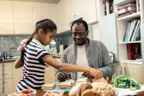Helpful daughter with nice hairstyle helping father in kitchen