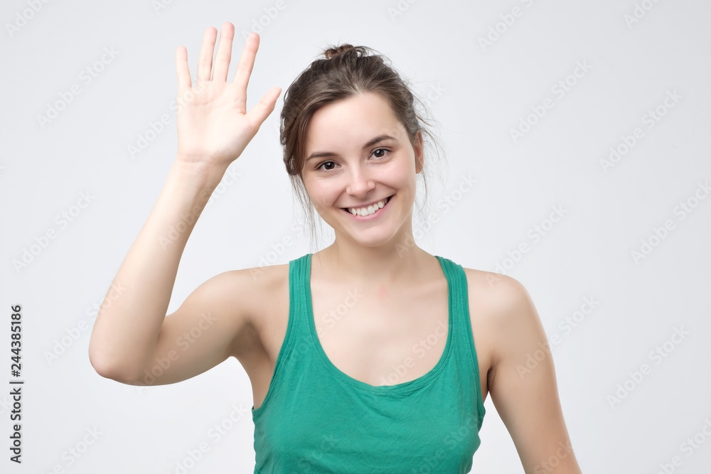 Pretty student girl saying hello, smiling joyfully and friendly, waving her hand Pretty student girl saying hello, smiling joyfully and friendly, waving her hand