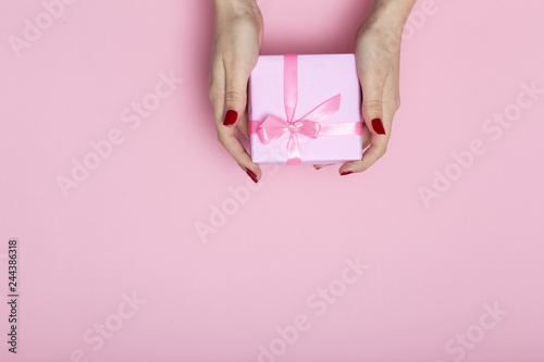 girl holding a present in hands, women giving a gift box wrapped in decorative paper on a pastel pink background, top view, concept holiday