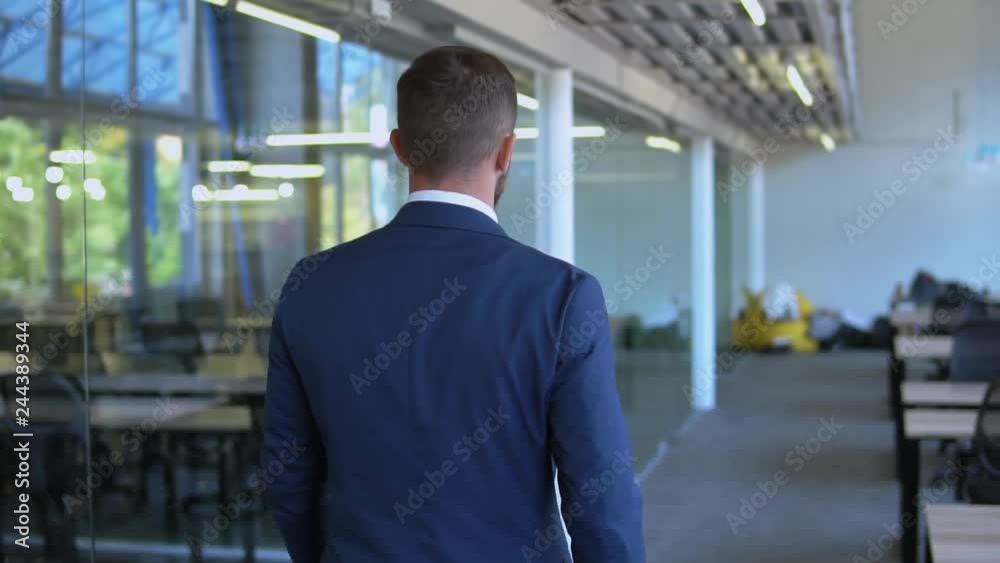back view business man wearing formal blue suit walking in open space office. employee walks in mobern lobby