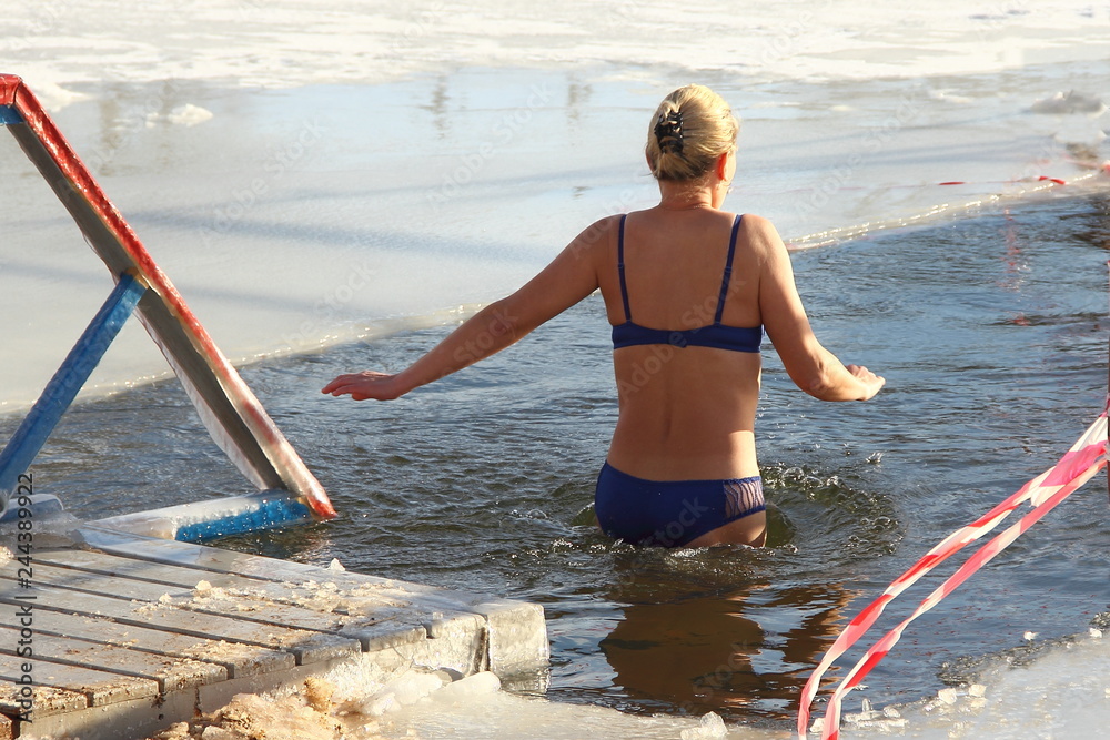 Beautiful walrus woman in swimsuit swimming in cold water in the ice hole in winter - winter sports, healthcare, HLS, , view from the back