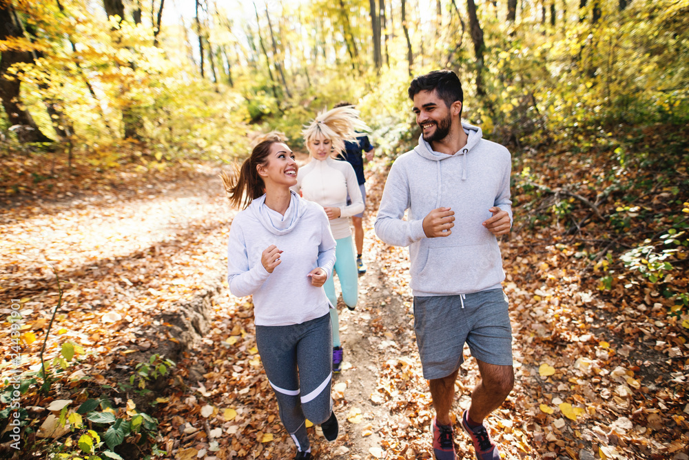Small group of people running in woods in the autumn. In foreground couple smiling at each other. Small group of people running in woods in the autumn. In foreground couple smiling at each other.