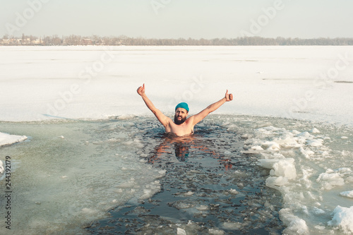 bearded man in hat in ice hole swimming