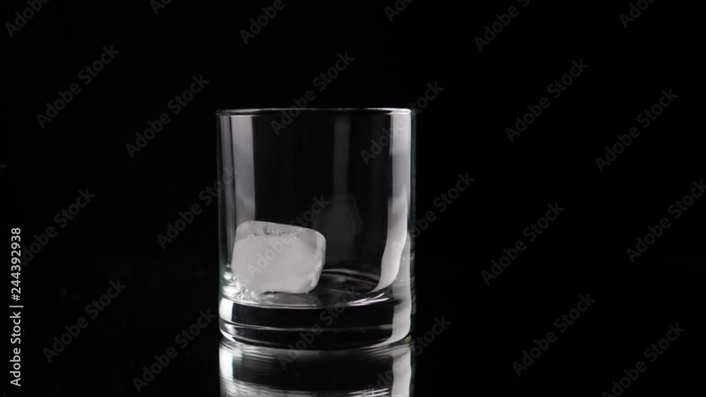 Ice cube falling into empty glass in slow motion. Partly real time, partly slow motion. Shallow depth of field Ice cube falling into empty glass in slow motion. Partly real time, partly slow motion. Shallow depth of field