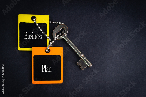 BUSINESS PLAN inscription written on wooden tag and key on black background with selective focus and crop fragment. Business and education concept