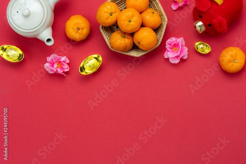 Chinese language mean rich or wealthy and happy.Table top view Lunar New Year & Chinese New Year concept background.Flat lay orange in basket and pig doll toy kid with cup of tea drink on red paper.
