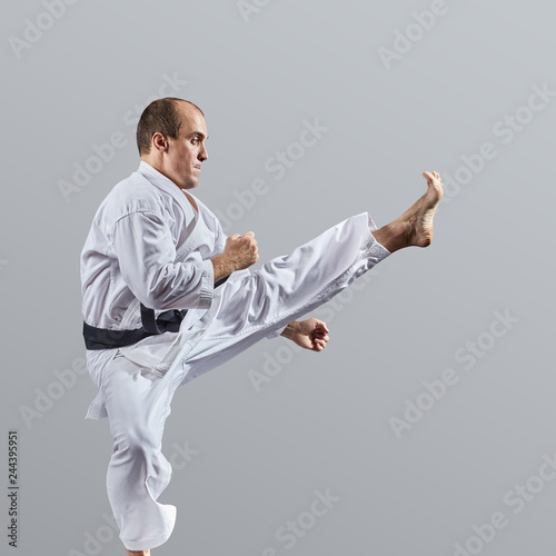 Adult man trains direct kick on a gray background