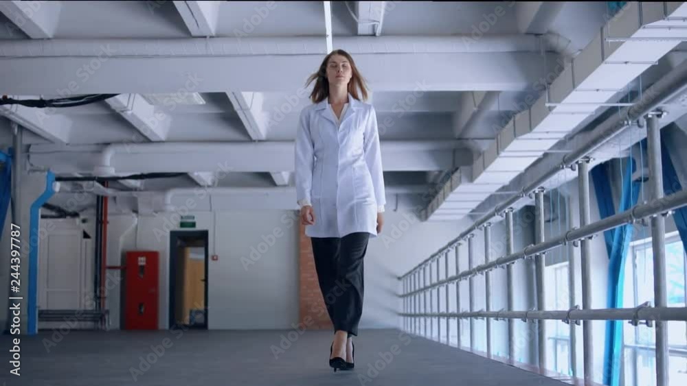 successful caucasian woman wearing white lab coat goes through the factory. successful caucasian woman wearing white lab coat goes through the factory.