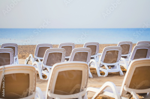 Summer morning empty sunny beach with white plastic chairs for sunbathing. Happy summer vacations concept. Horizontal color image. © Andrii Oleksiienko