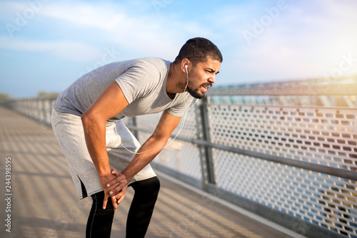 Young athlete having problem with his knee during training. Sportsman feeling pain in his knees while running. Sports injuries and health concept. photo