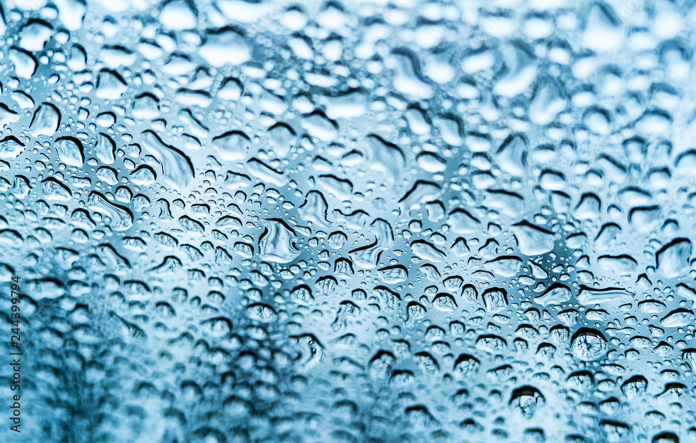 Different drops of rain on a glass surface with light blue background. Water drops for background and design. Close-up Different drops of rain on a glass surface with light blue background. Water drops for background and design. Close-up