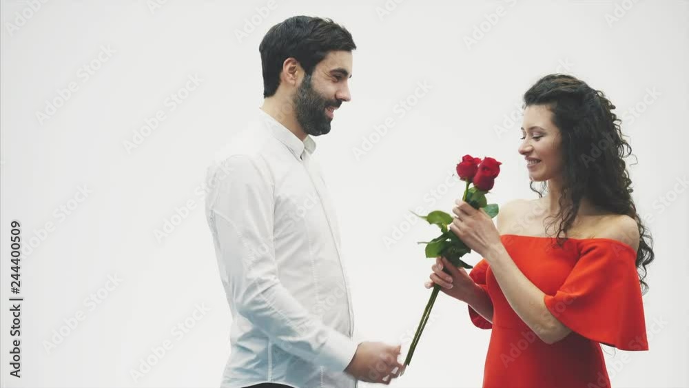 Beautiful romantic couple isolated on white background. An attractive young woman wearing red roses in a dress and a beautiful man in a white shirt gives the rose with love and tenderness. Valentine's Beautiful romantic couple isolated on white background. An attractive young woman wearing red roses in a dress and a beautiful man in a white shirt gives the rose with love and tenderness. Valentine's
