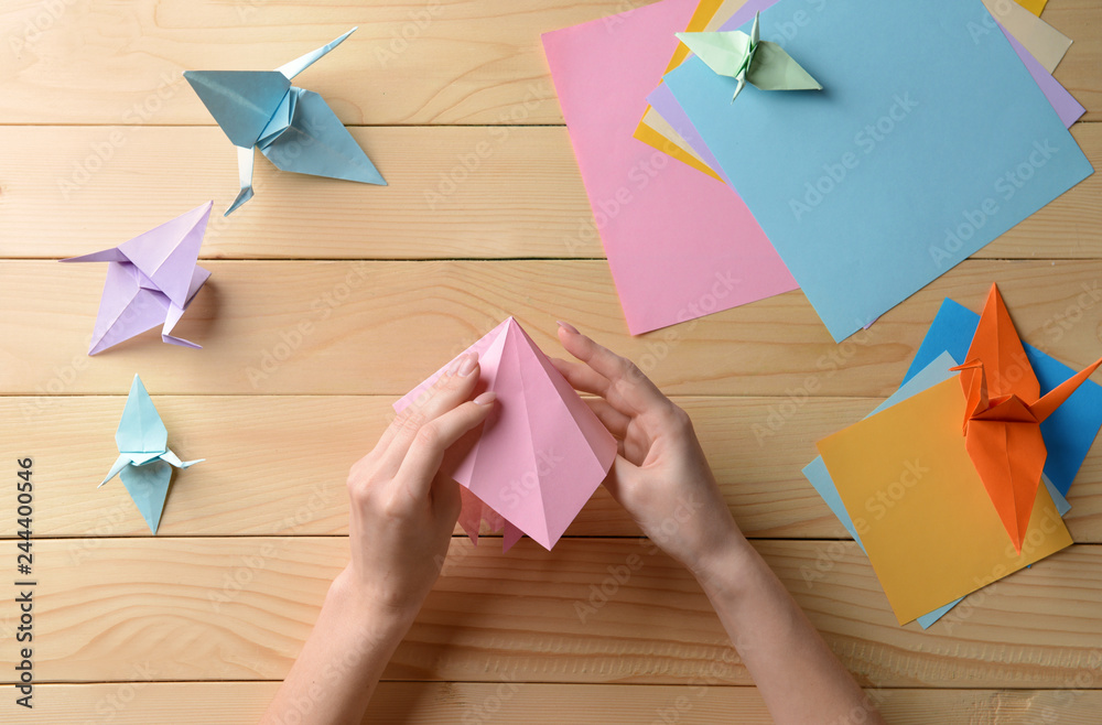 Young woman making origami on wooden table - obrazy, fototapety, plakaty 