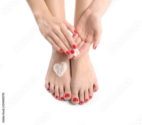 Young woman with beautiful pedicure applying cream on white background