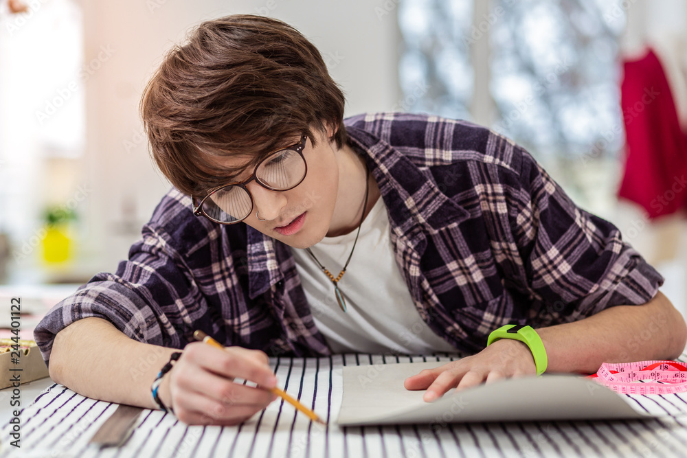Young dark-haired asian designer in a checkered shirt looking busy Young dark-haired asian designer in a checkered shirt looking busy