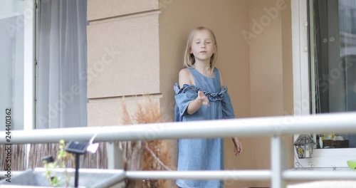 A nice blond girl is standing on the balcony and sending an air kiss.