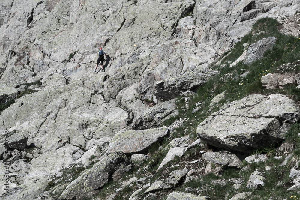 Woman walker climbing waymarked trail to alpine pass in summer