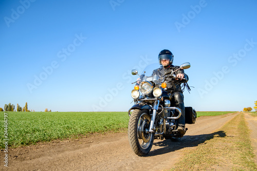 Motorcycle Driver Riding Custom Chopper Bike on Autumn Dirt Road in the Green Field. Adventure Concept.