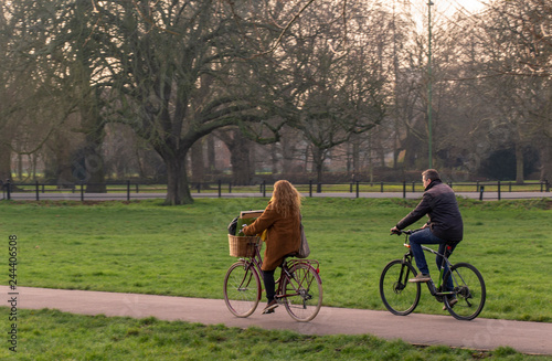 couple cycling through city park rapped up warm on a bright winter evening