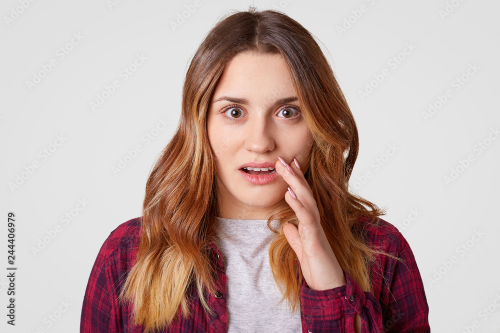 Headshot of surprised young woman looks with astonishment, has wavy hair, scared of something horrified, has appealing appearance, models against white background. Facial expressions concept Headshot of surprised young woman looks with astonishment, has wavy hair, scared of something horrified, has appealing appearance, models against white background. Facial expressions concept