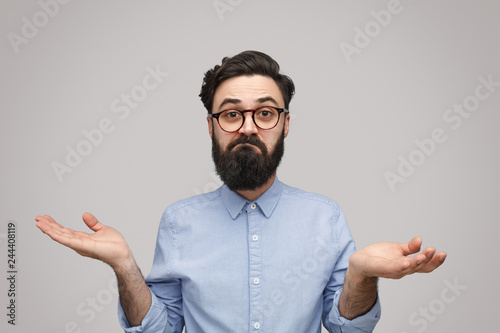 Doubtful bearded man shrugging with shoulders