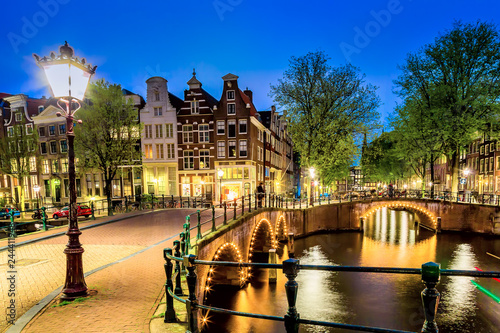 Amsterdam canal with typical dutch houses and bridge during twilight blue hour in Holland, Netherlands.