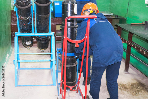 Photography A worker in a helmet is loading a gas oxygen cylinder onto a trolley at an indus
