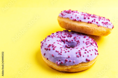 Two delicious lilac donuts with sprinkle on bright yellow background