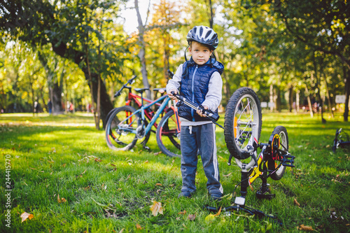 Subject child and profession. A little blond Caucasian boy uses a bicycle pump, pumps air into a tire wheel bicycle, a child repairs a bicycle in a meadow in a park in autumn