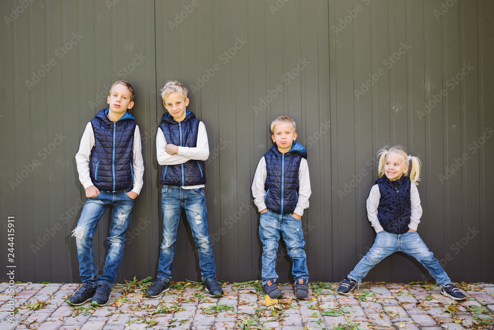 Funny Caucasian big family of three brothers and sister posing standing on  growth background of wall