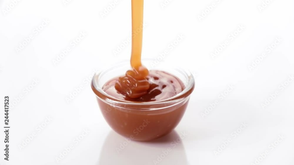 Melted caramel flowing in glass bowl on white background Melted caramel flowing in glass bowl on white background