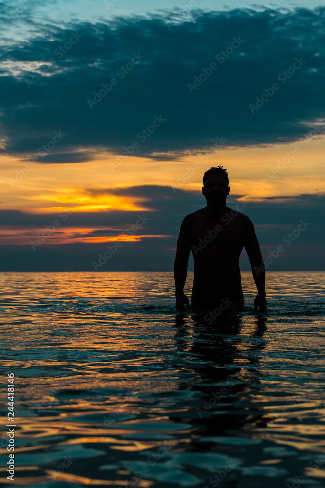 Guy walking out from the beach under sunset.