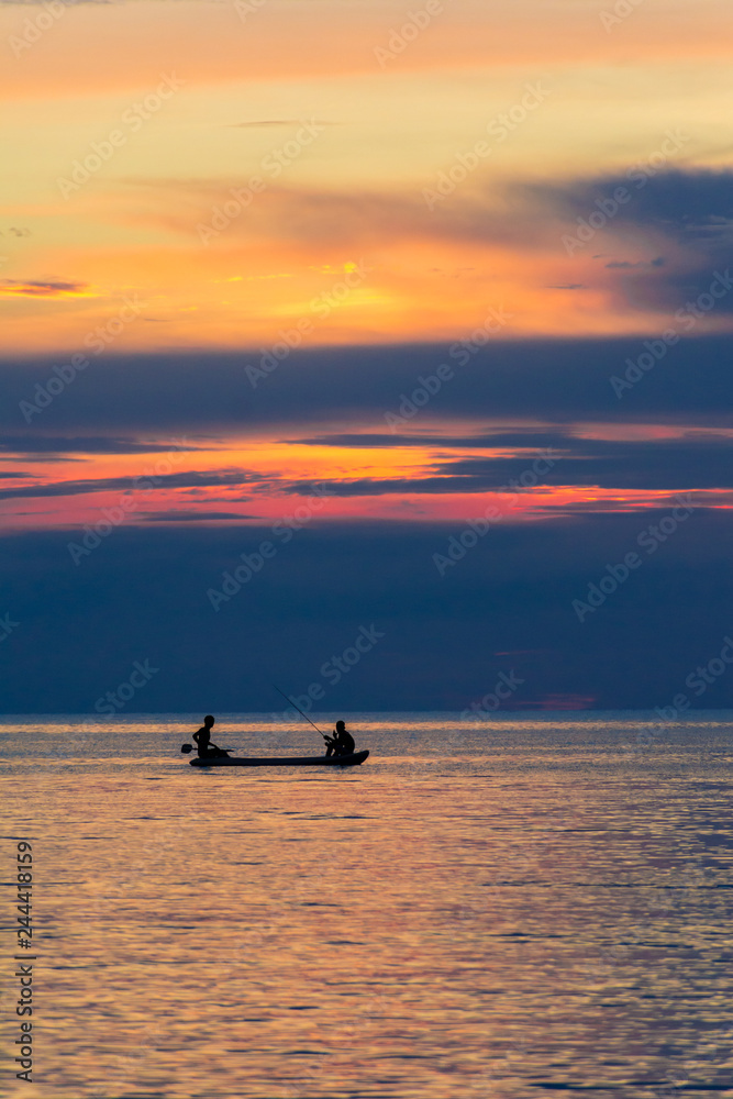 Two men fishing on the sea under sunset.