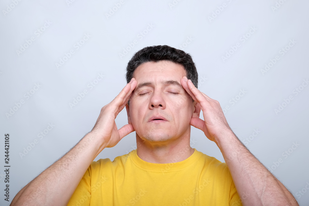 White middle-aged man with closed eyes touching his head with two hands White middle-aged man with closed eyes touching his head with two hands