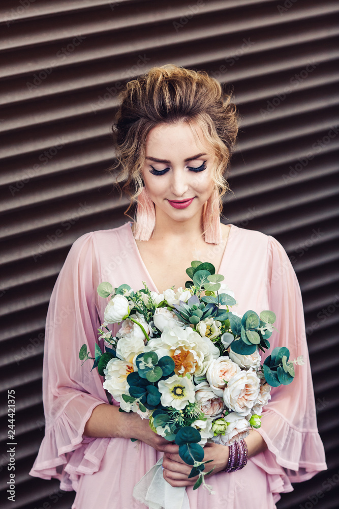 attractive young girl in a short dress with a bouquet of flowers posing near the granite wall with rolling shutters. attractive young girl in a short dress with a bouquet of flowers posing near the granite wall with rolling shutters.