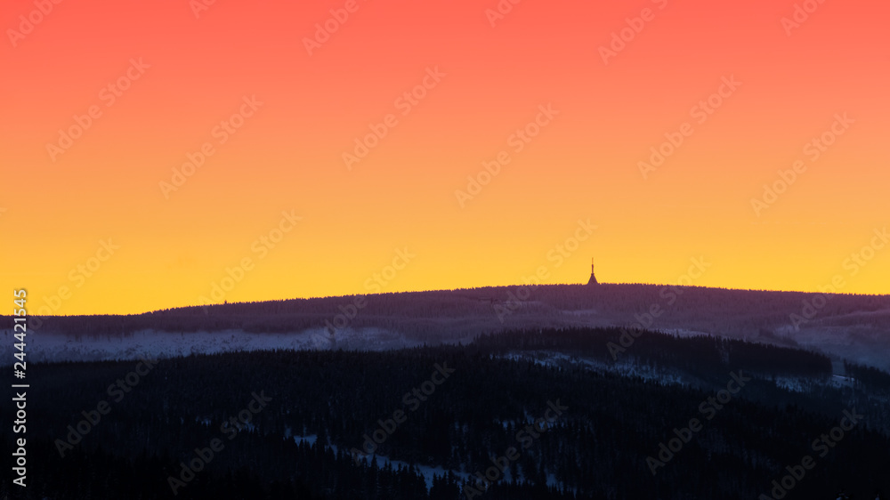Beautiful sunset with wooden and snowy mountains with transmitter tower on the highest peak and colorful golden red sky, Cerna hora (Schwarzenberg), Krkonose (Giant Mountains), Czech Republic